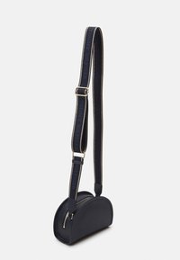 Námořnická kůže crossbody taška s oblým tvarem, zlatým zipem a nastavitelným popruhem se znakem a kontrastním prošíváním.