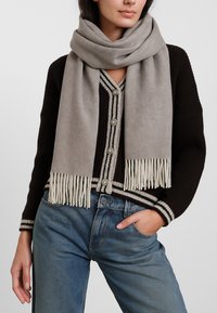 Sciarpa di lana grigia con frange, tessuto morbido, avvolta intorno al collo. Abbinata a un cardigan nero con leggere strisce e bottoni.