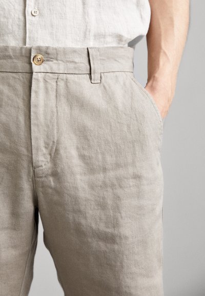 Pantalon en lin beige clair avec une coupe décontractée, doté d'une fermeture à bouton, de poches latérales et d'un tissu doux et texturé.