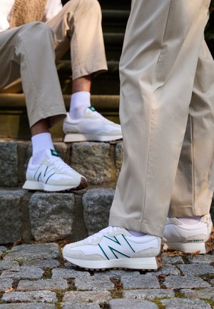 Dwie osoby w beżowych spodniach i białych butach sportowych New Balance stoją i siedzą na kamiennych schodach na zewnątrz.