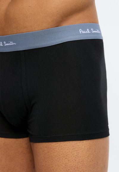 Κοντινό πλάνο ενός ατόμου που φοράει μαύρα ανδρικά εσώρουχα Paul Smith με γκρι λάστιχο μέσης που φέρει το λευκό λογότυπο της μάρκας.