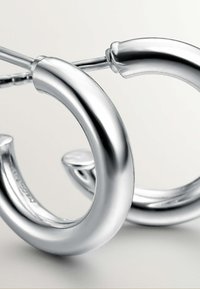 Pendientes de argolla de plata con una superficie lisa y reflectante, que presentan un diseño redondeado y un cierre sin costuras para facilitar su uso.