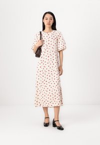 Kruidige midi-jurk in crème met korte pofmouwen en een getailleerde taille. Gecombineerd met zwarte glanzende hakken en een kleine bruine handtas.