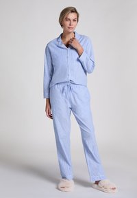 Ensemble de pyjama rayé bleu et blanc comprenant un haut à boutons avec col et un pantalon à taille élastique, accompagné de pantoufles beiges duveteuses.