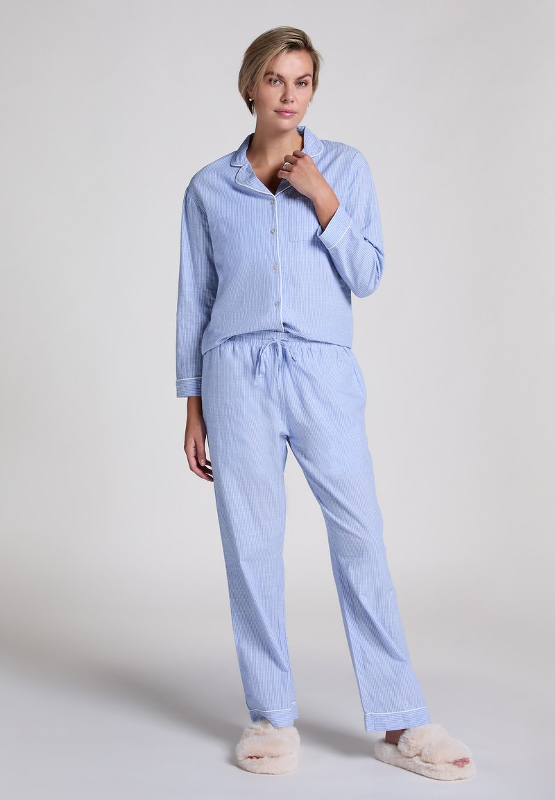 Ensemble de pyjama rayé bleu et blanc comprenant un haut à boutons avec col et un pantalon à taille élastique, accompagné de pantoufles beiges duveteuses.
