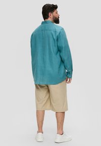 Turquoise linnen shirt met een kraag, met knoopmanchetten; gecombineerd met beige shorts. Witte sneakers maken de casual outfit compleet.