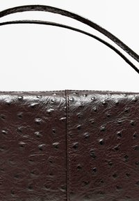 Brun läderhandväska med strukturerad yta, prydd med upphöjda prickar, rektangulär form och två smala handtag för bärning.