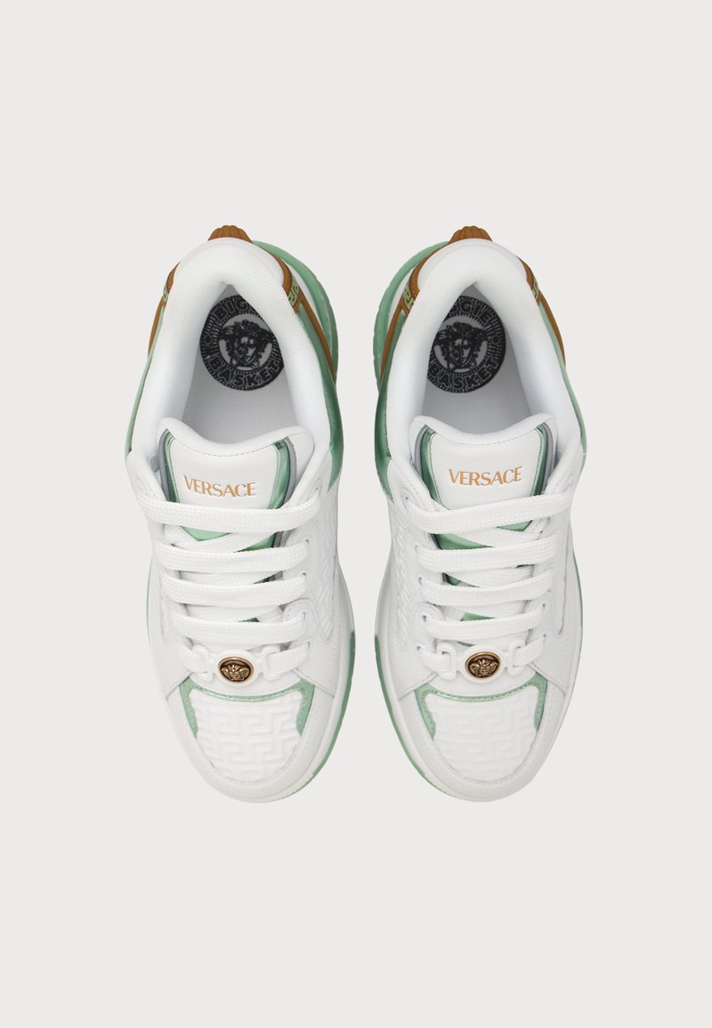 Pair of white Versace sneakers with green and gold accents, gold Medusa emblem near laces, and Versace logo on tongue, viewed from above.
