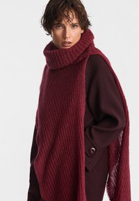 Bordowy, oversize sweter wykonany na drutach z wysokim ściągaczem, z długim, teksturowanym detalem przypominającym szal oraz luźnym krojem.