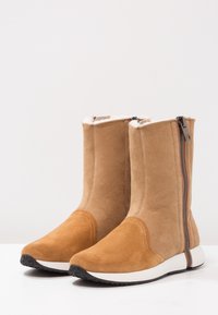 Botas de tobillo de gamuza color topo con un diseño elegante, cremallera lateral y suela de goma blanca. Textura suave con un detalle de costura mínimo.