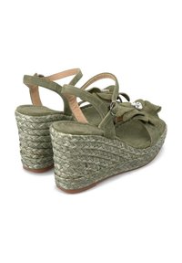 Sandali platform in finta suede verde con design avvolgente, tacco in iuta intrecciata e un fiocco decorativo con un accento di strass.