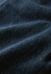 Tume sinine teksariidest kangas tekstuurse pinnaga, millel on õrnad heledad täpid ja pehmed voldid, rõhutades selle raskust ja langevust.