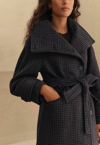 Wool blend coat in dark blue and brown houndstooth pattern, featuring a large collar, belted waist, rolled cuffs, and side pockets.