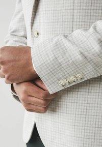 Hellgrauer kariertes Blazer mit einer strukturierten Oberfläche, ausgestattet mit einem Ein-Knopf-Verschluss und vier dekorativen Knöpfen am Ärmel.