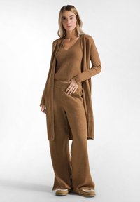 Conjunto de ropa de hogar de punto marrón que incluye un cárdigan largo, una blusa de cuello en V y pantalones de pierna ancha. Textura suave con un corte relajado, adecuado para un atuendo casual.