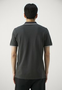 Polo shirt grigio scuro con colletto classico, maniche corte e dettagli bianchi al colletto e ai polsini. Texture del tessuto morbida.