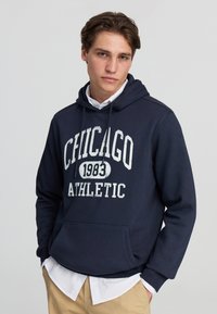 Felpa blu navy con stampa bianca "CHICAGO 1983 ATHLETIC". Materiale in misto cotone, tasca a marsupio e cappuccio con coulisse regolabile.