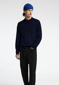 Maglione lavorato a maglia blu navy con scollo rotondo, abbinato a jeans neri. Accessoriato con un berretto in maglia a coste blu. Design semplice e moderno.