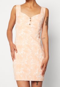 Brzoskwiniowa sukienka w kwiaty o dopasowanym fasonie, z kwadratowym dekoltem, szerokimi ramiączkami i trzema ozdobnymi guzikami z przodu. Gładka tekstura materiału.