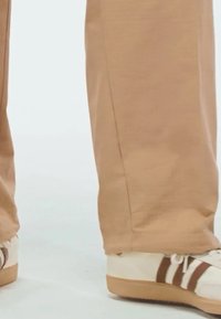 Pantalones anchos beige con una textura suave, combinados con zapatillas blancas que tienen rayas marrones y suela de goma.
