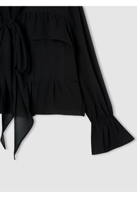 Blusa nera realizzata in un tessuto leggero e fluido. I dettagli principali includono strati con rouches, un fiocco al collo e maniche a campana.