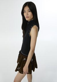 Top sin mangas negro con cuello alto y acentos metálicos, combinado con una falda marrón bordada con cintura ajustable.