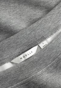 Grijze stof top met een gladde textuur. Het label toont het merk "NOELLA", maat S, met een gestikte naaddetail. Simpel en minimalistisch ontwerp.