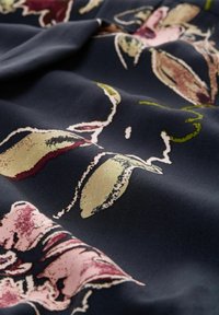 Tessuto blu navy con un motivo floreale in rosa e verde. Il tessuto ha una consistenza liscia, che mette in mostra dettagli intricati nel design stampato.