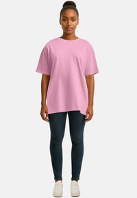T-shirt rosa oversize in morbido tessuto con maniche corte, abbinata a jeans blu scuro e sneakers bianche, caratterizzata da una vestibilità comoda e un colletto rotondo.