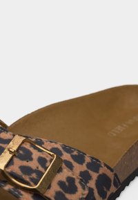 Κοντινό πλάνο ενός σανδαλιού με λουράκι σε σχέδιο λεοπάρδαλης και χρυσή πόρπη, με καφέ πάτο και μαύρη σόλα.