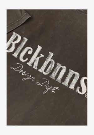 Brauner Stoff mit kräftigem, abgenutztem weißen Text "Blckbnn's Design Dept." Glatte Textur mit leichtem Glanz.