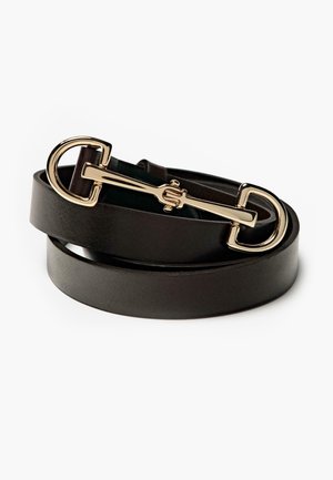 Ceinture en cuir noir enroulée avec une boucle de style mors de cheval en or sur fond blanc.
