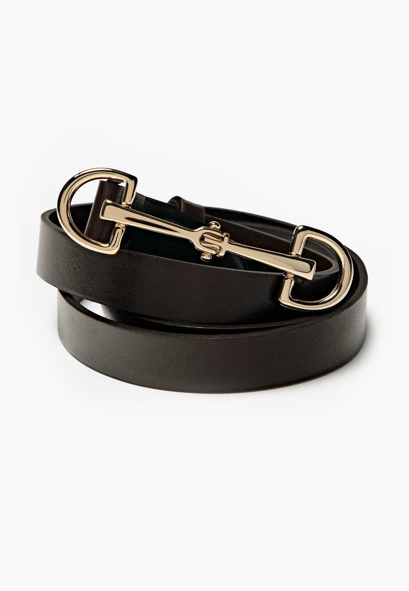 Ceinture en cuir noir enroulée avec une boucle de style mors de cheval en or sur fond blanc.