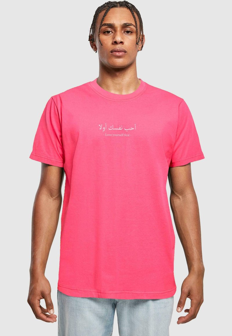 Camiseta de algodón rosa con mangas cortas, que presenta texto en árabe y la frase en inglés "Ámate a ti mismo primero", centrada en el pecho.