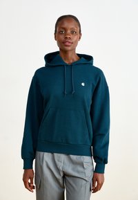 Dark teal hoodie made of soft fabric, featuring a front pocket, drawstring hood, and a small white logo on the left chest. Paired with gray pants.