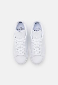 Baskets blanches avec une finition en cuir lisse, bout rond, design lacé, languette et col rembourrés, avec un logo sur la semelle intérieure.