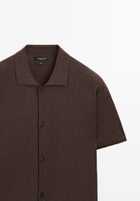 Camicia marrone a maniche corte con bottoni e colletto, realizzata in cotone, mostrata su uno sfondo bianco semplice.