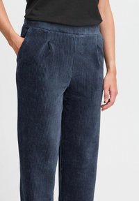 Granatowe sztruksowe spodnie o pionowym prążkowaniu, z bocznymi kieszeniami i luźnym krojem. Pas gładki z subtelnymi zakładkami.