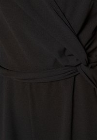 Črn material s gladko, zloženo teksturo, ki vsebuje zasukano zasnovo pri pasu in natančno šivano pasnico.