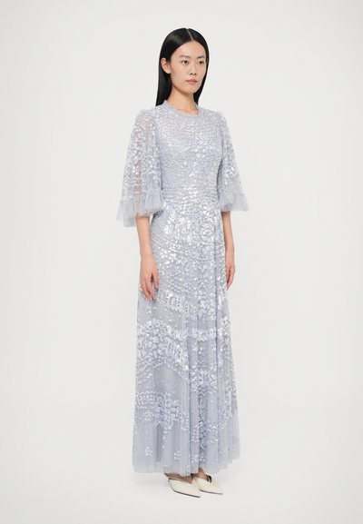 Μάξι φόρεμα από ανοιχτό μπλε τούλι με παγέτες, με κοντά φουσκωτά διαφανή μανίκια και λουλουδένια σχέδια, συμπληρωμένο με μυτερές άσπρες γόβες.