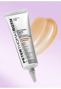 Un tube argenté avec une pointe contient un gel beige clair. Le texte inclut le nom du produit, les instructions d'utilisation et le volume. L'arrière-plan est d'un rose doux.