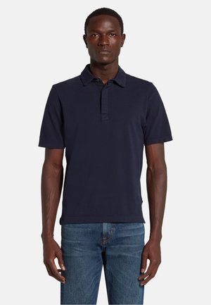 Marineblaues Poloshirt aus Baumwolle mit lockerer Passform, kurzen Ärmeln und einer Knopfleiste mit drei Knöpfen. Kombiniert mit Jeans.