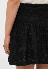 Saia preta bordada com uma cintura franzida, apresentando um design em camadas e padrões intrincados semelhantes a renda, destacando uma superfície texturizada.