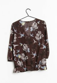 Brun blomstret bluse med V-hals, trekvartlange ærmer, flæset kant og et fuglemønster i blå, gul og hvid på en gennemsigtig stof.