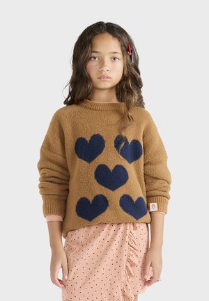 Brązowy sweter robiony na drutach z granatowymi wzorami serc, z okrągłym dekoltem i ściągaczami, połączony z różową spódnicą w kropki z falbanami.