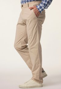 Beige byxor i lättviktsmaterial med avslappnad passform. Har sidofickor och knäppning med knapp, tillsammans med vita sneakers.