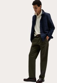 Niebieska lniana koszula, kremowy polo, zielone plisowane spodnie i ciemnobrązowe mokasyny. Koszula ma kolorowy kołnierzyk oraz guziki.