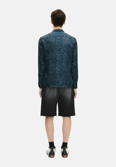 Het shirt heeft een blauw luipaardprintpatroon, lange mouwen en een klassieke kraag. Gepaarde met zwarte shorts en sneakers met witte accenten.