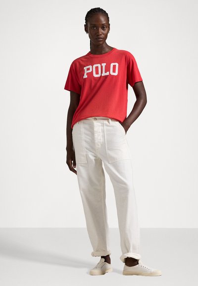 Tricou roșu cu mâneci scurte, având inscripția "POLO" în litere albe; asortat cu pantaloni largi de culoare crem și adidași bej.