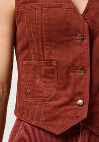 Vest din corduroy de culoare ruginită, cu decolteu în V, butoane frontale și o buzunar decorativ cusut cu un design în zigzag.